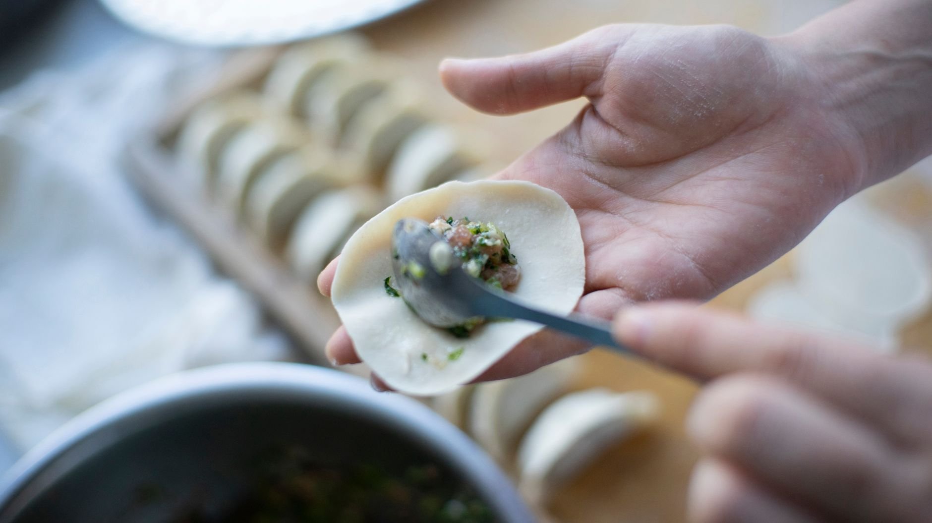 Hands crafting dumplings by hand — filling placed carefully into rolled dough on a floured table