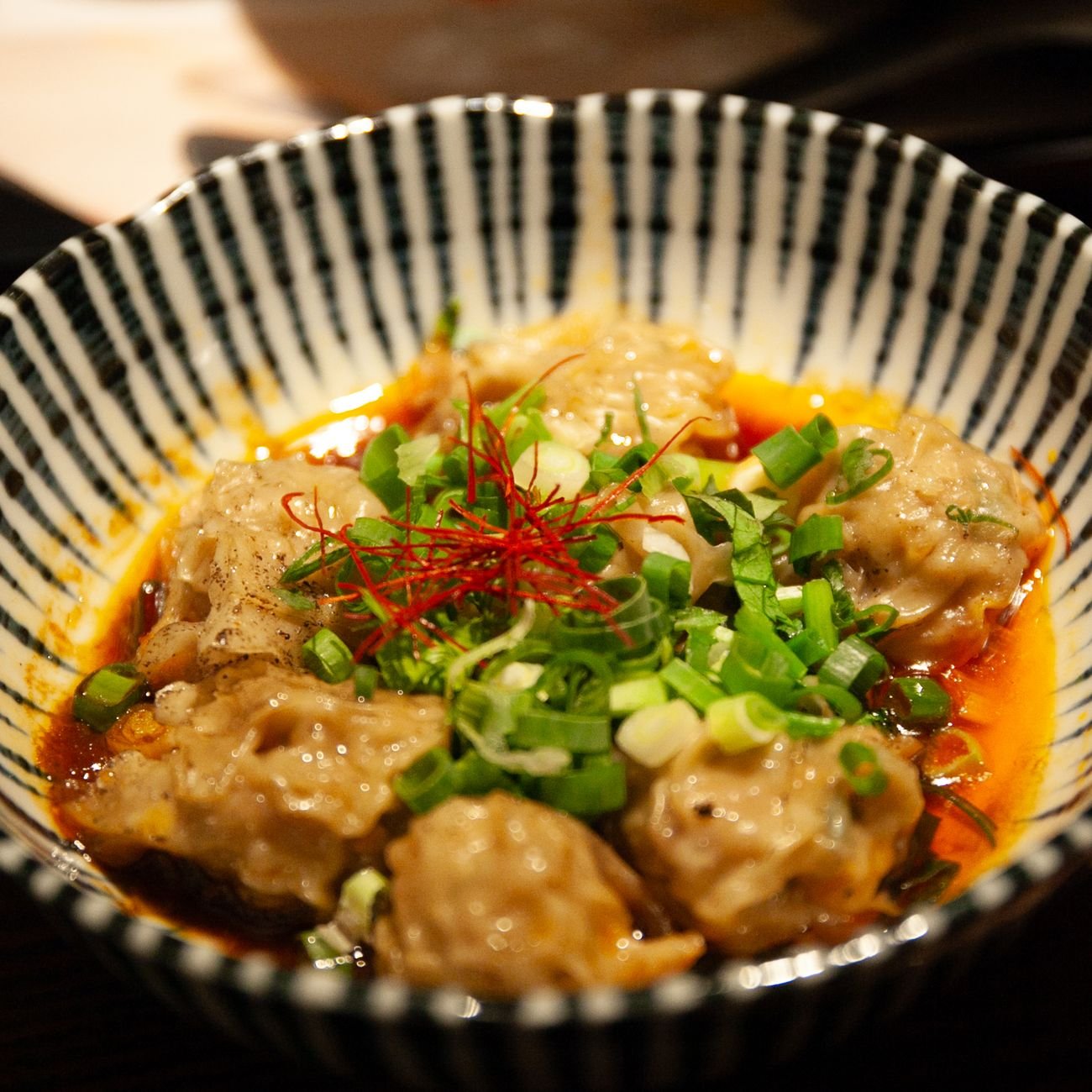 Delicious spicy dumplings garnished with green onions and chilli strands in a bowl